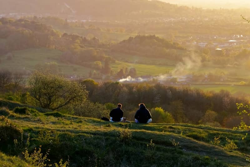 Two people sit on a hill at sunset.