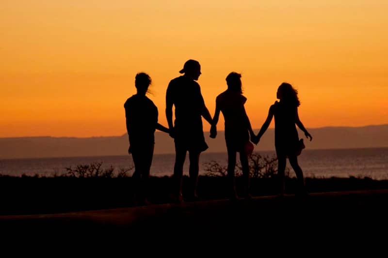 A family in silhouette holding hands against a warm orange sky by the sea