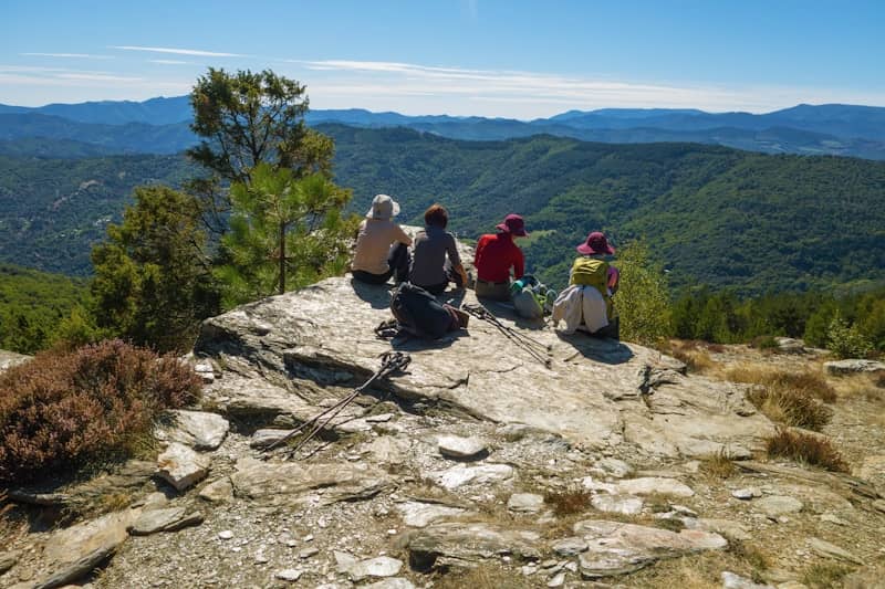 Four hikers resting on a rocky mountain summit overlooking hills.