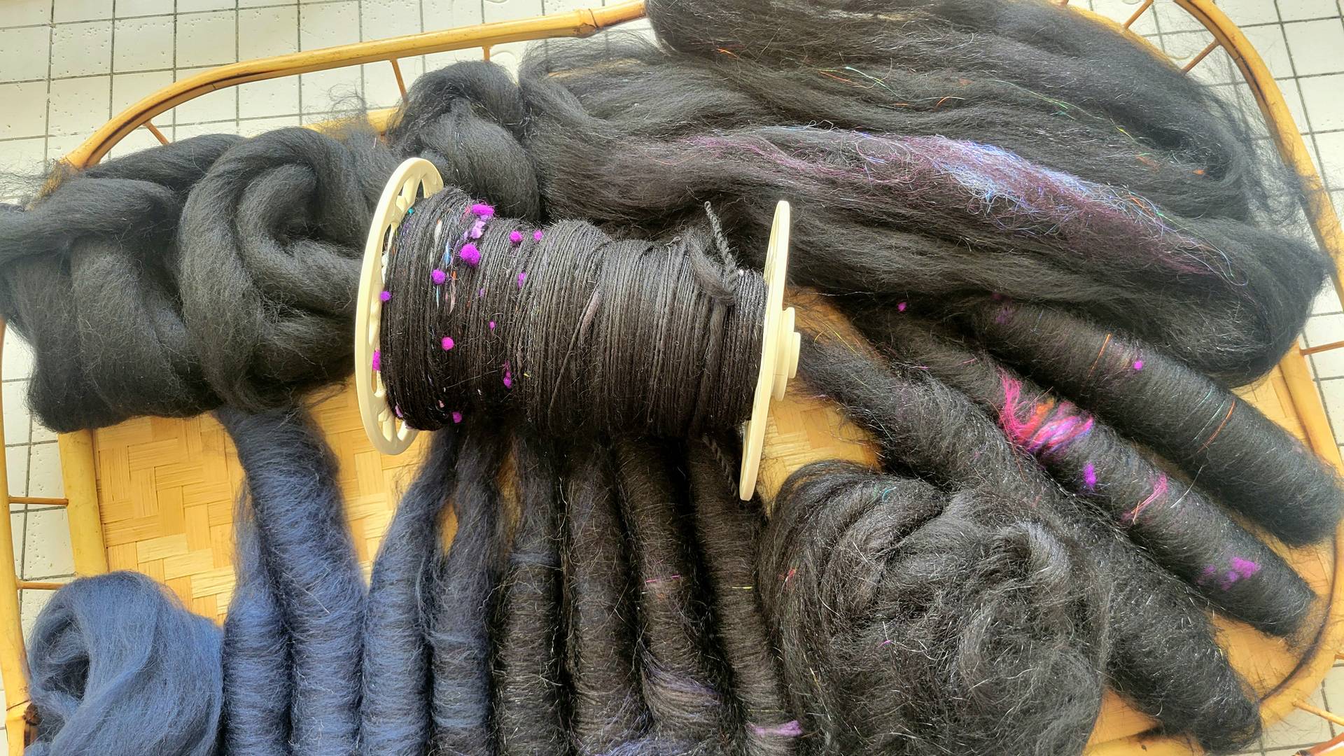 Black singles on a bobbin laying atop the fiber and rolags prepared for spinning the second singles.