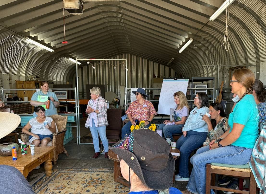 Group of women sitting in a circle talking inside a metal building.