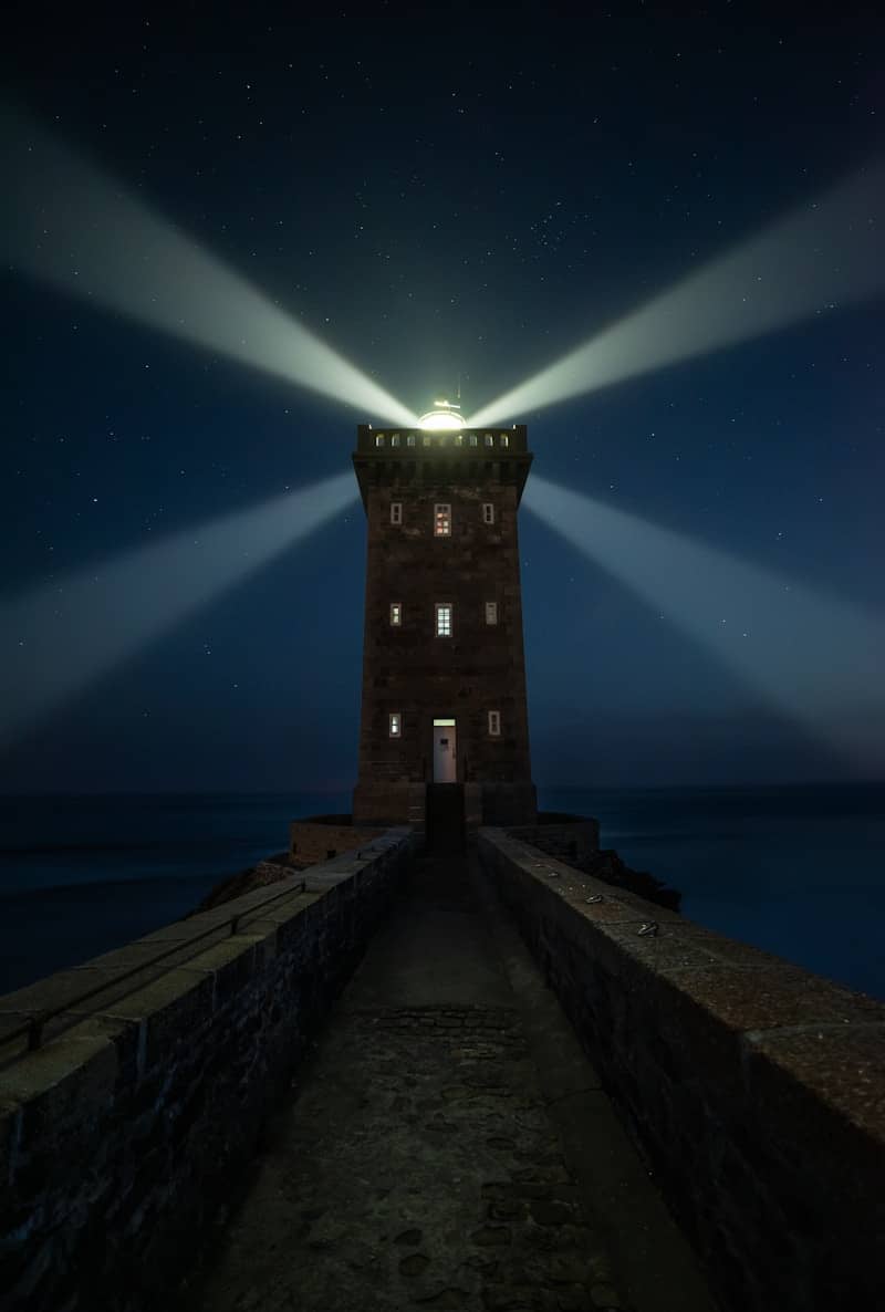 Lighthouse beam sweeps across the starry night sky