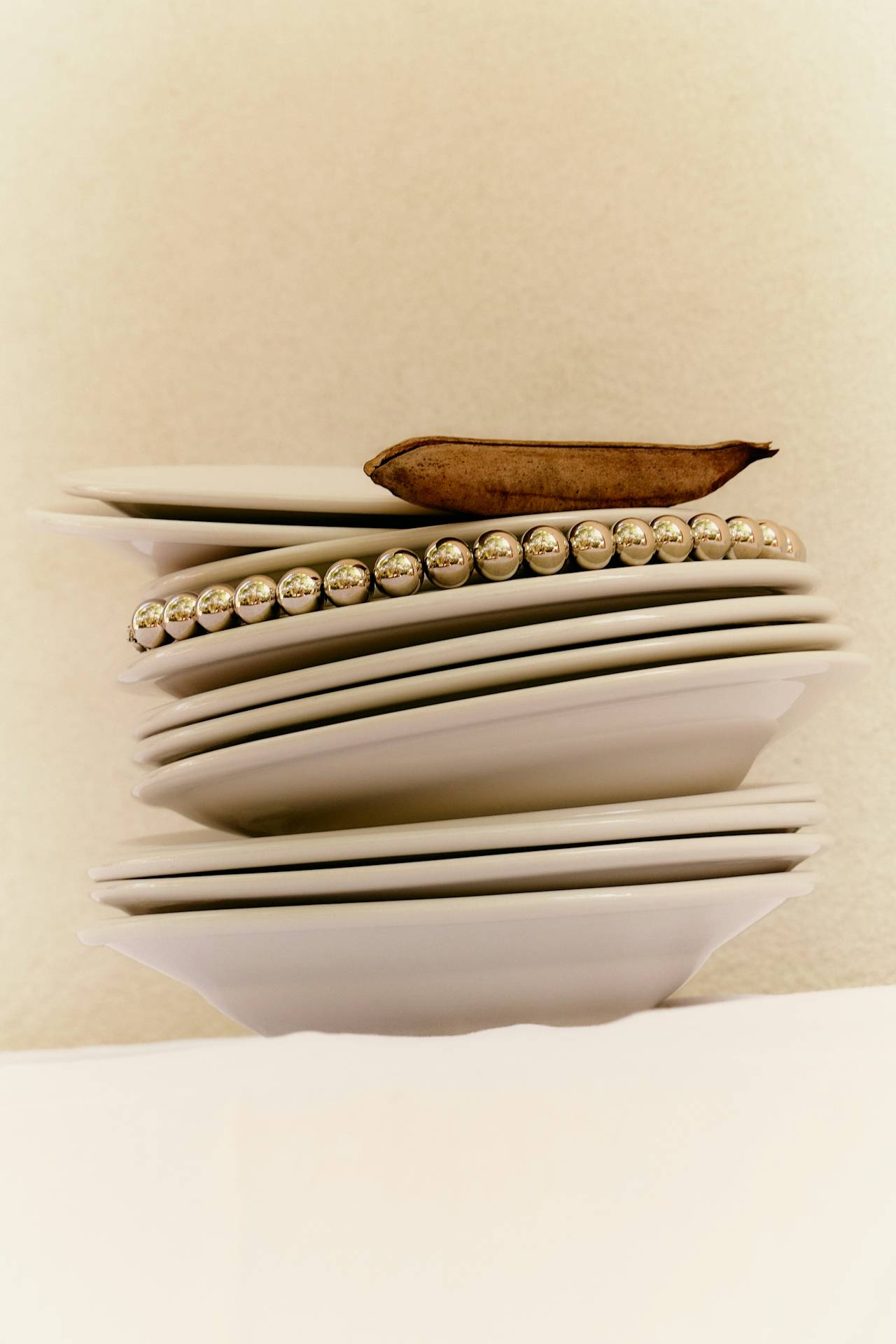 A pile of white bowls and dishes, a pearl necklace wrapped around one of the dishes