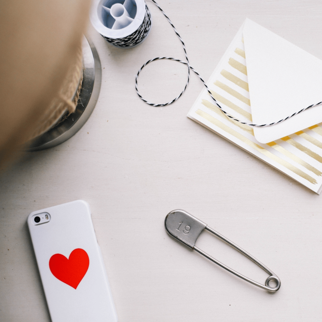 A desktop containing a safety pink, a card and envelope, and a white phone with a red heart on its case