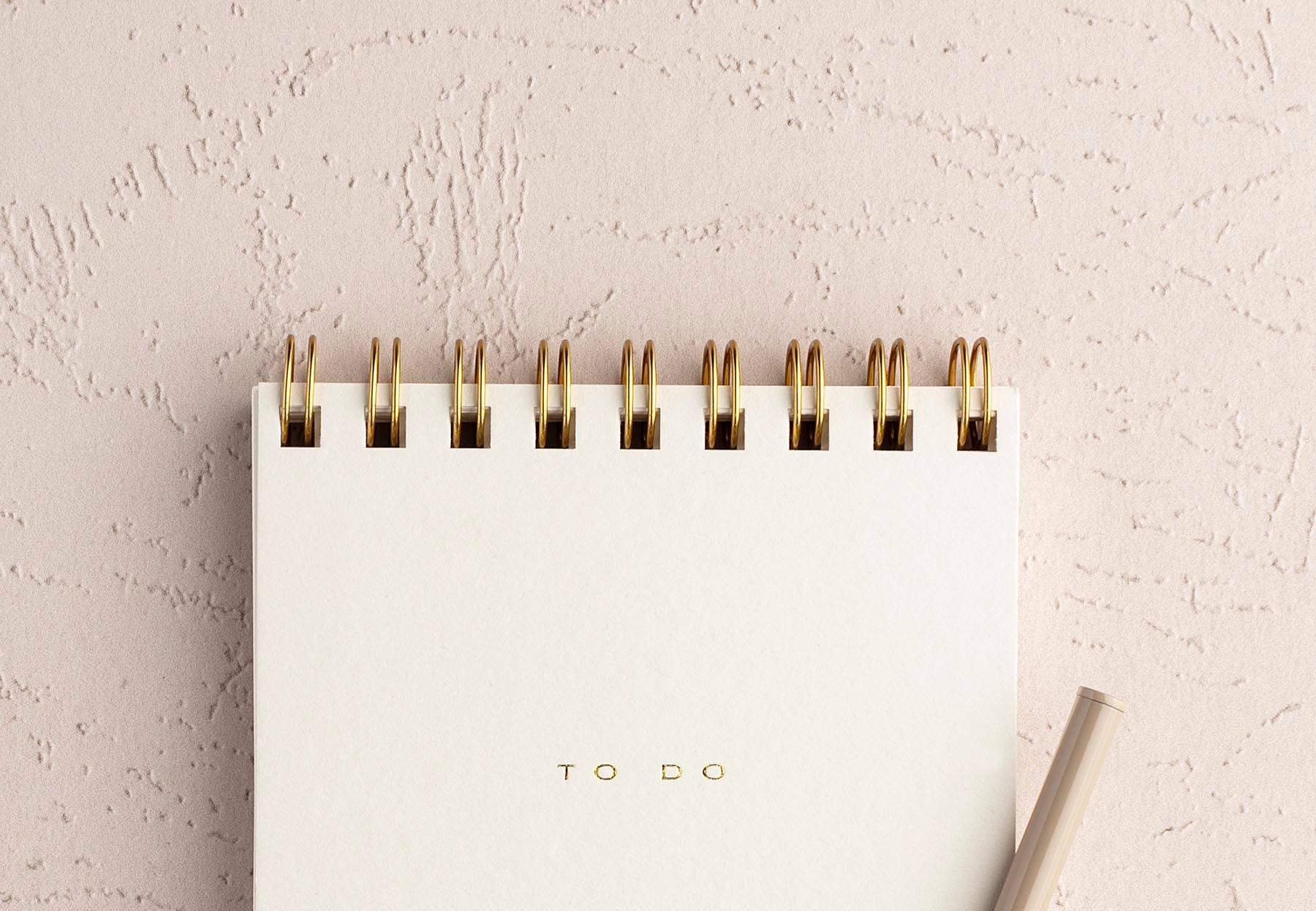 a pen and notepad with "to do" on the cover on a textured stucco-like surface