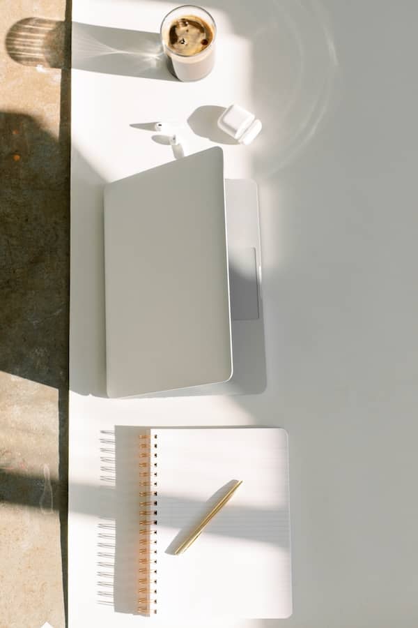 a laptop and notebook sit on a sunlit desk