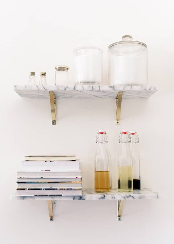 two kitchen shelves with canisters of flour, sugar, jars of vinegar, and a stack of cookbooks