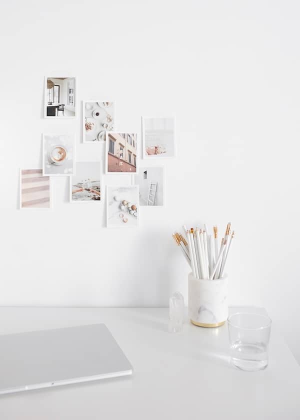 a mug full of white pencils on a desk with a moodboard of photos taped to the wall behind it