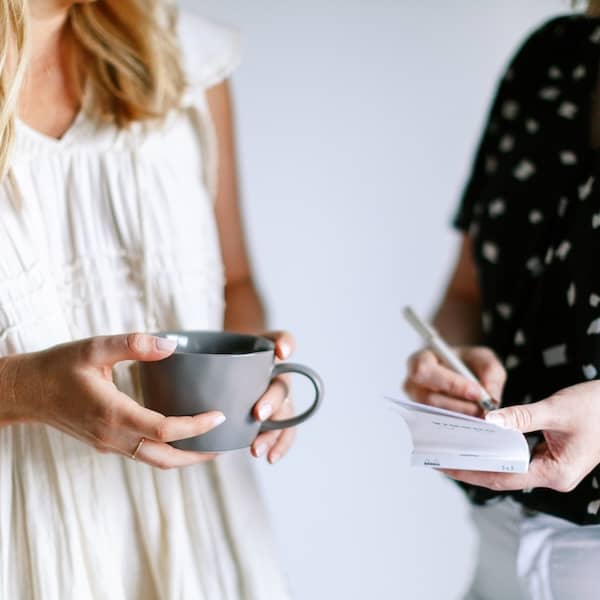 a brand strategy consultant takes notes while standing beside a client holding a mug of coffee