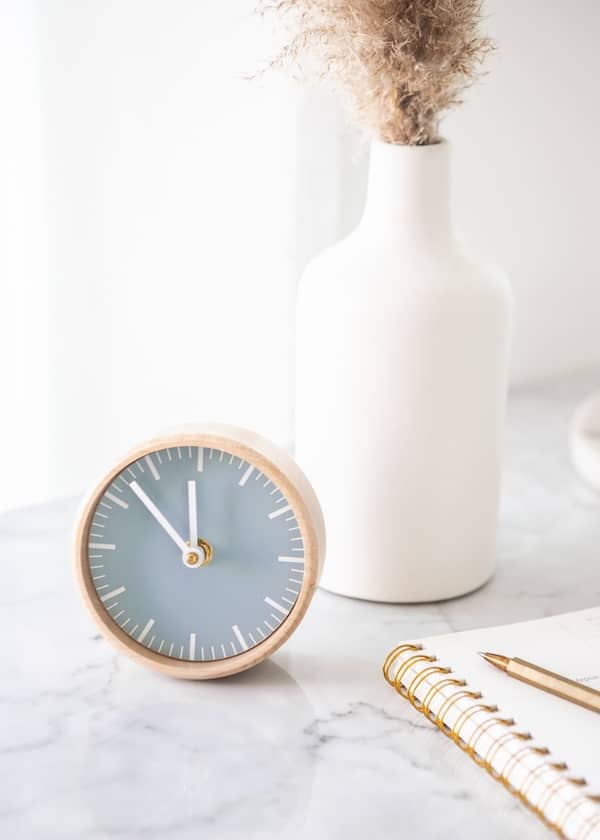 a clock sits on a marble desk with a white vase in the background
