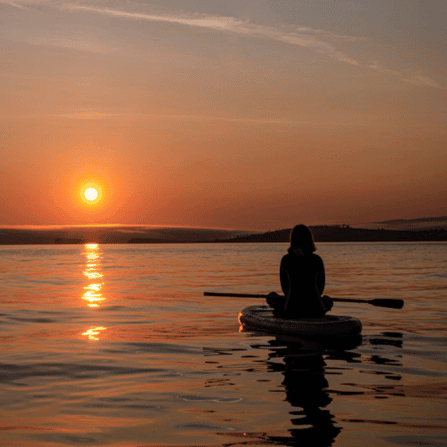 person sitting on paddle board at sunset