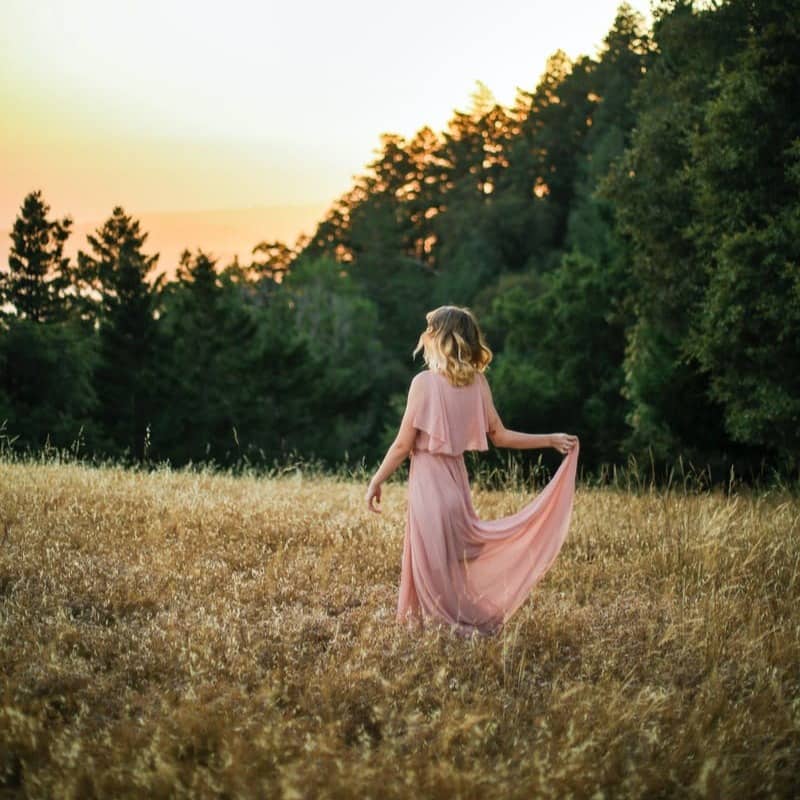 woman in pink dress standing on brown grass field during daytime