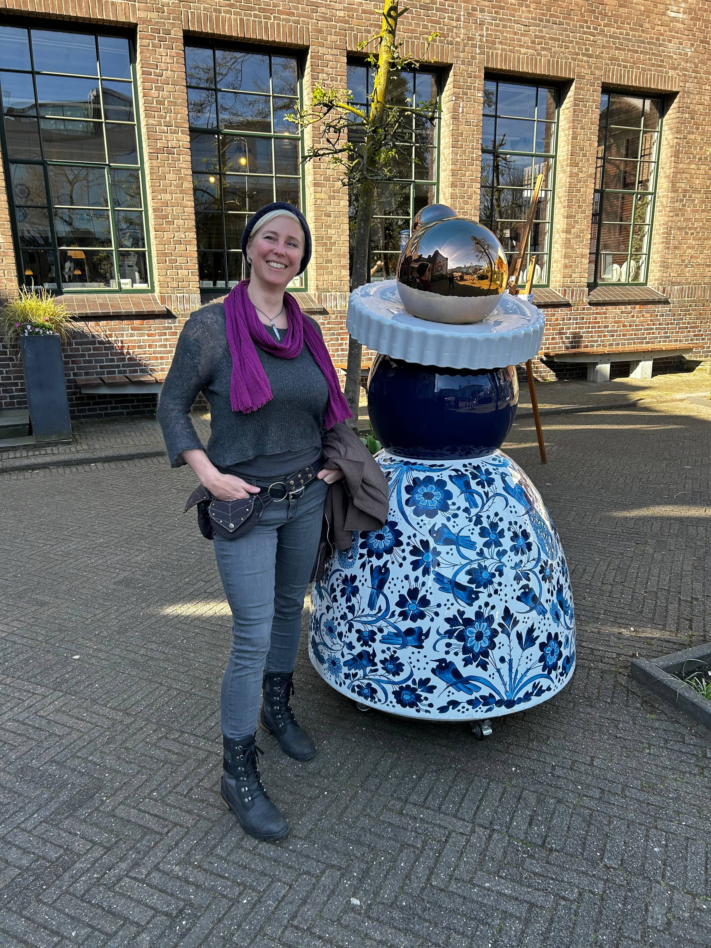 Jessie stands next to a ceramic Proud Mary figurine: bell-shaped skirt painted in Delft blue flowers, a ceramic ruff collar, and a shiny silver head.