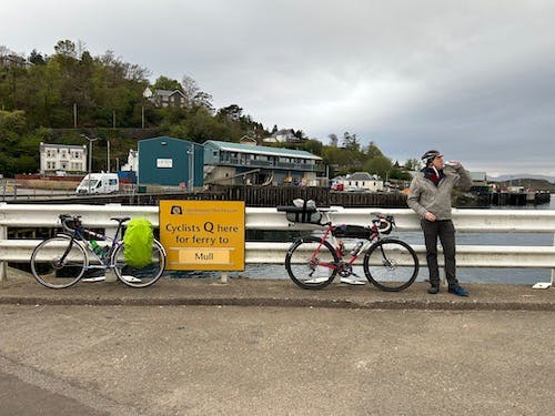 Two bicycles parked by a sign that reads "Cyclists Queue here for ferry to Mull." Robert poses beside them