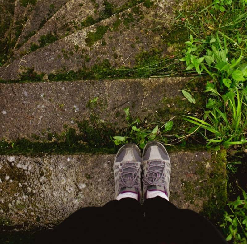 Person's feet on old mossy concrete stairs surrounded by grass.