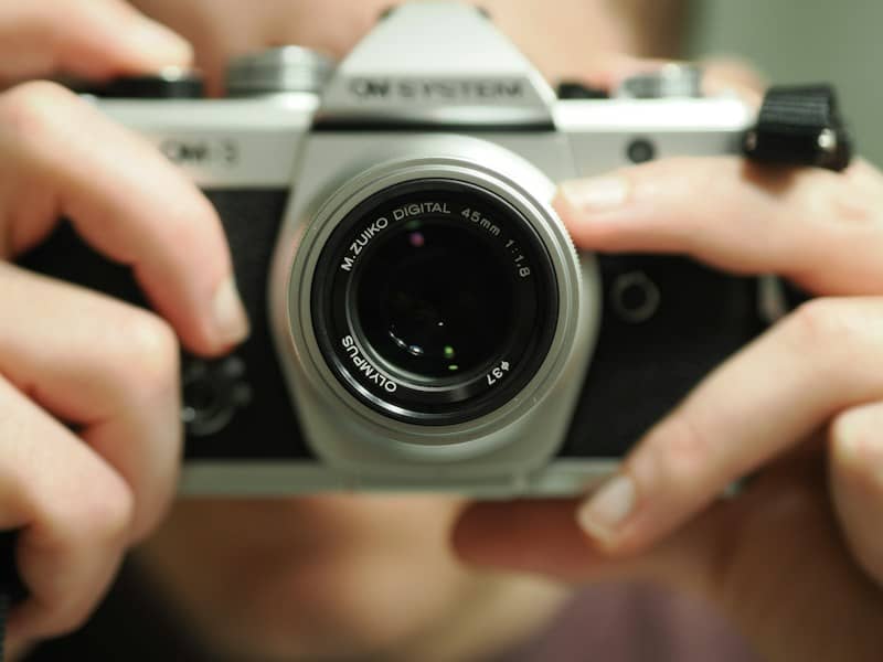 Vintage silver camera held by hands, lens prominent.