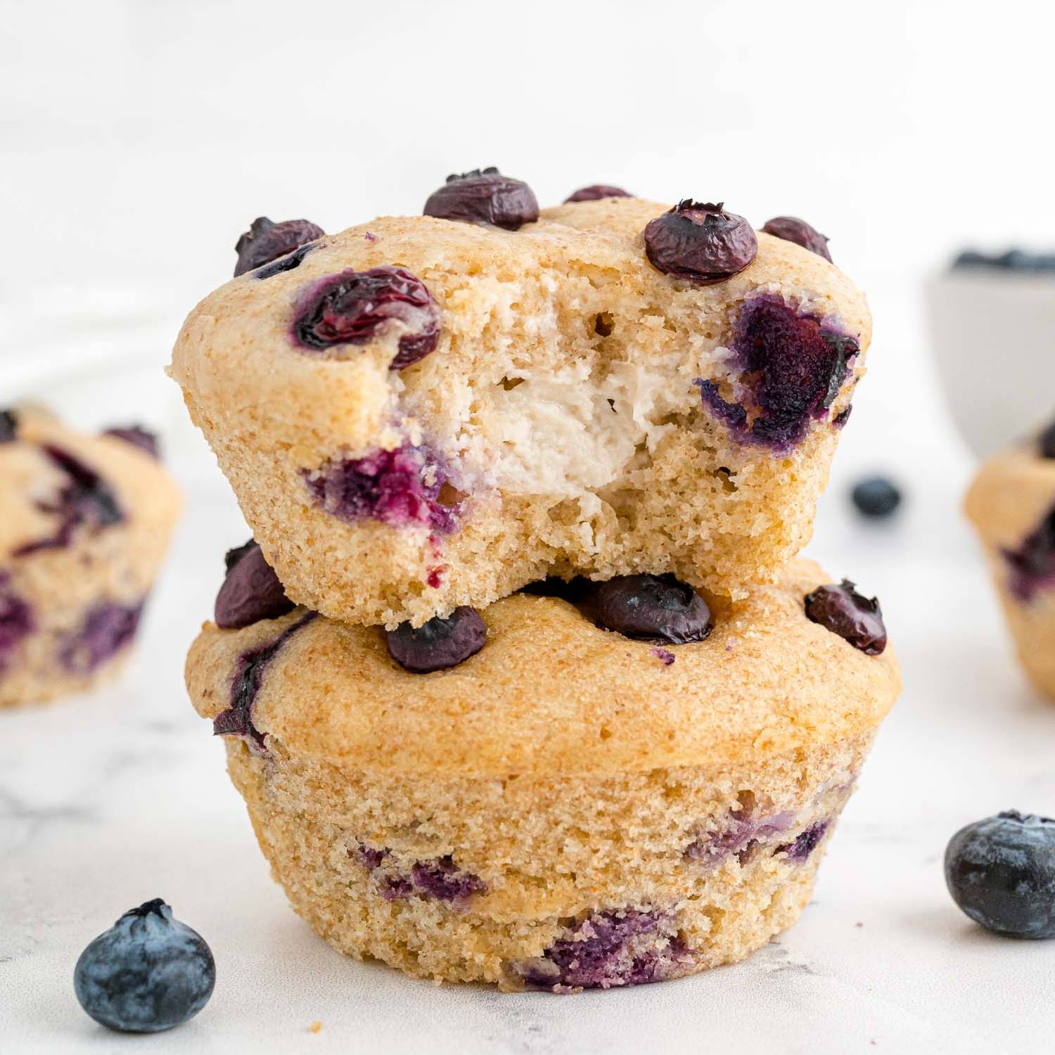 Blueberry cream cheese muffins, two stacked on top of each other, the top one with a bite removed.