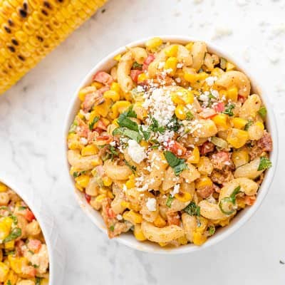Pasta salad with macaroni noodles, corn, cilantro, and cotija cheese, in a small bowl.
