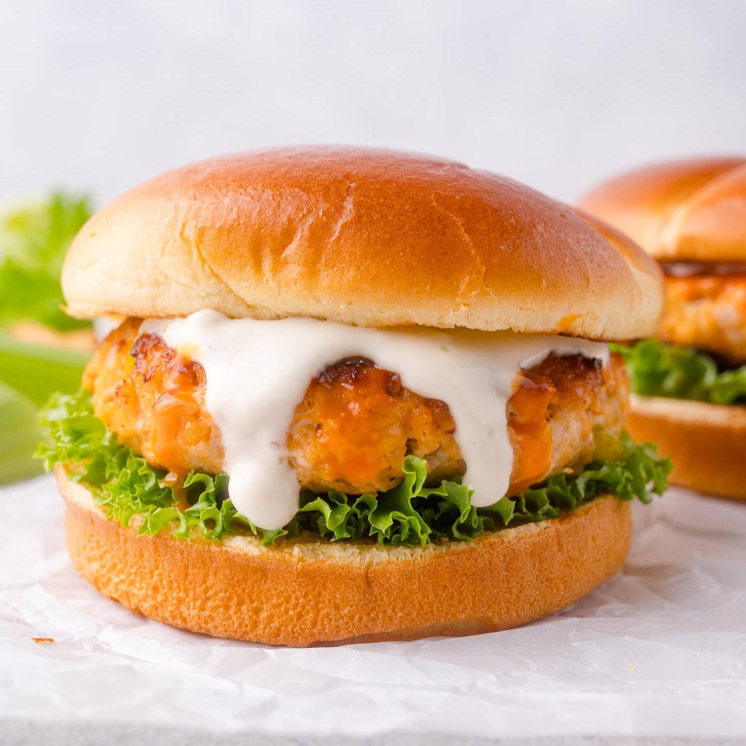 Chicken burger with buffalo sauce on a bun with lettuce and ranch.