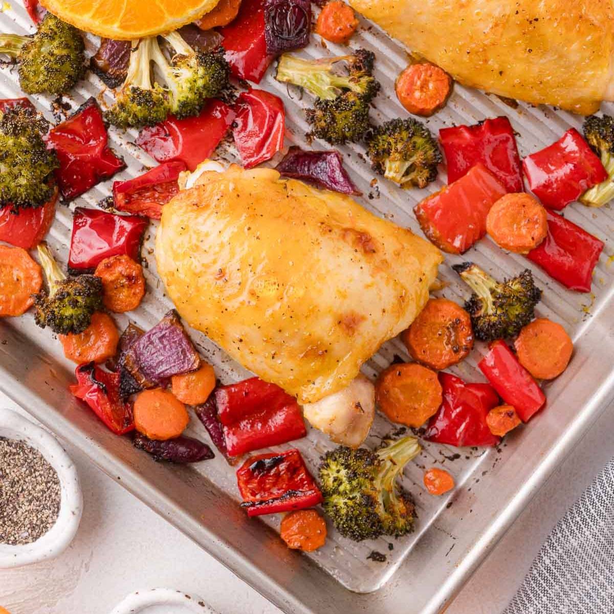 Chicken thighs on a sheet pan with colorful vegetables.