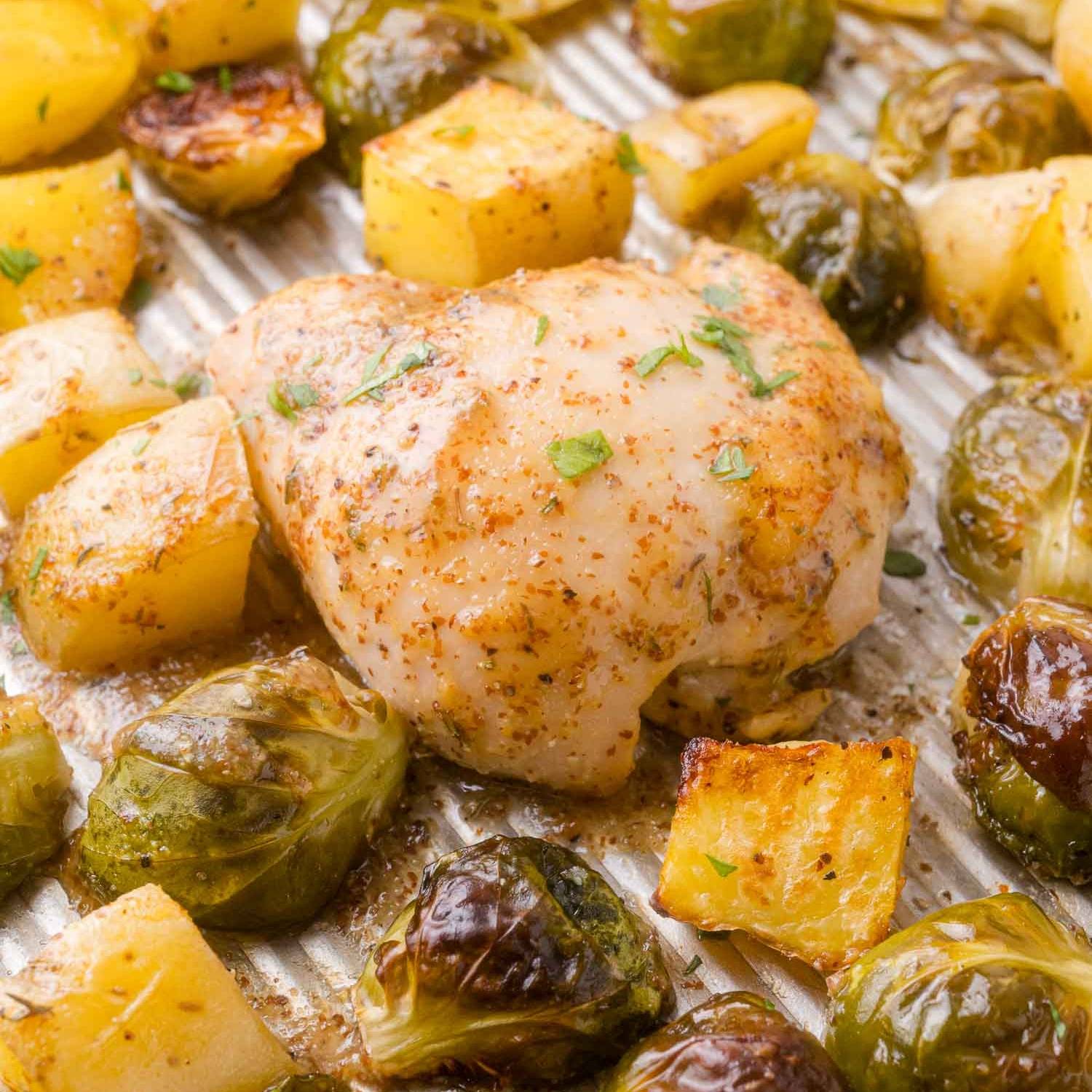 Cooked boneless chicken thigh on a pan with roasted Brussels sprouts and potatoes, all with a mustard glaze.