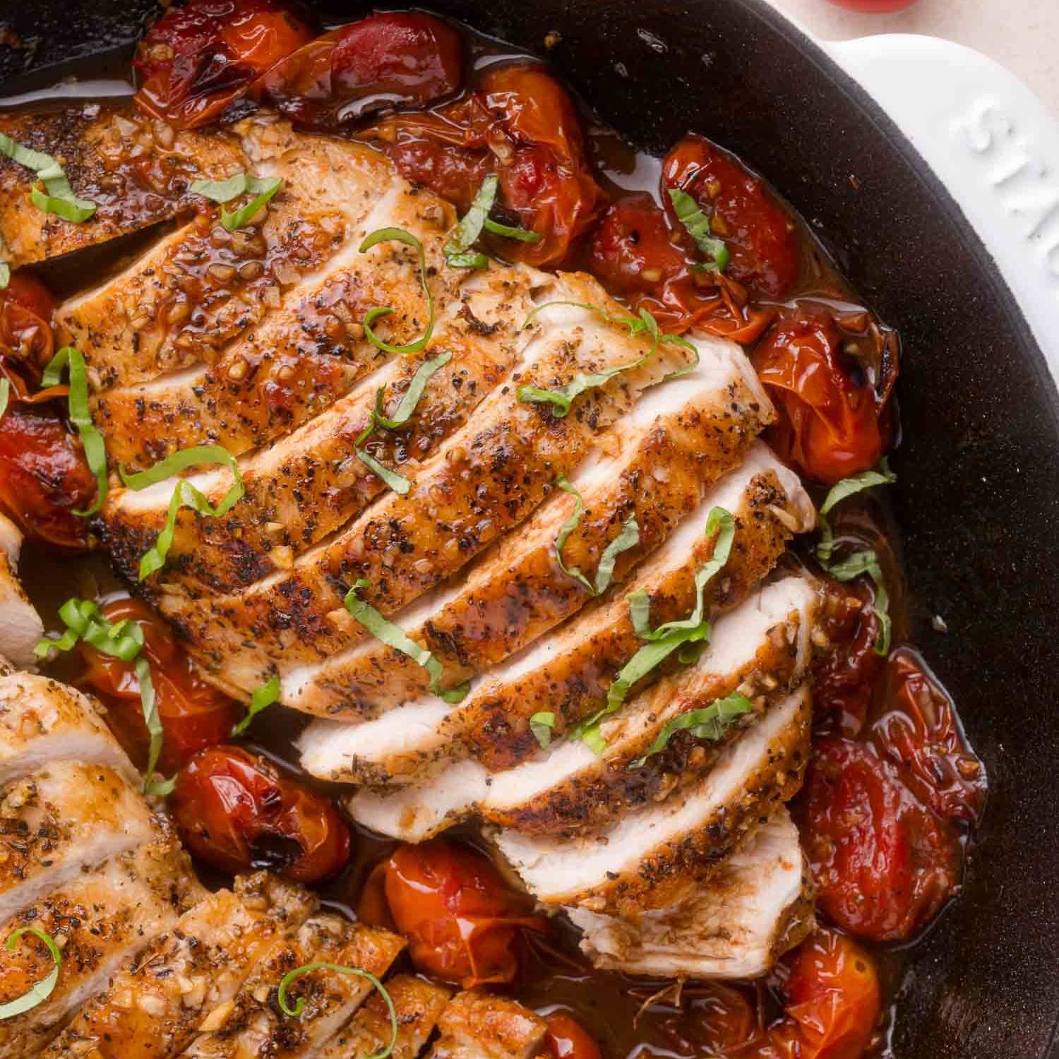 Sliced cooked chicken on a bed of roasted tomatoes, topped with fresh basil.