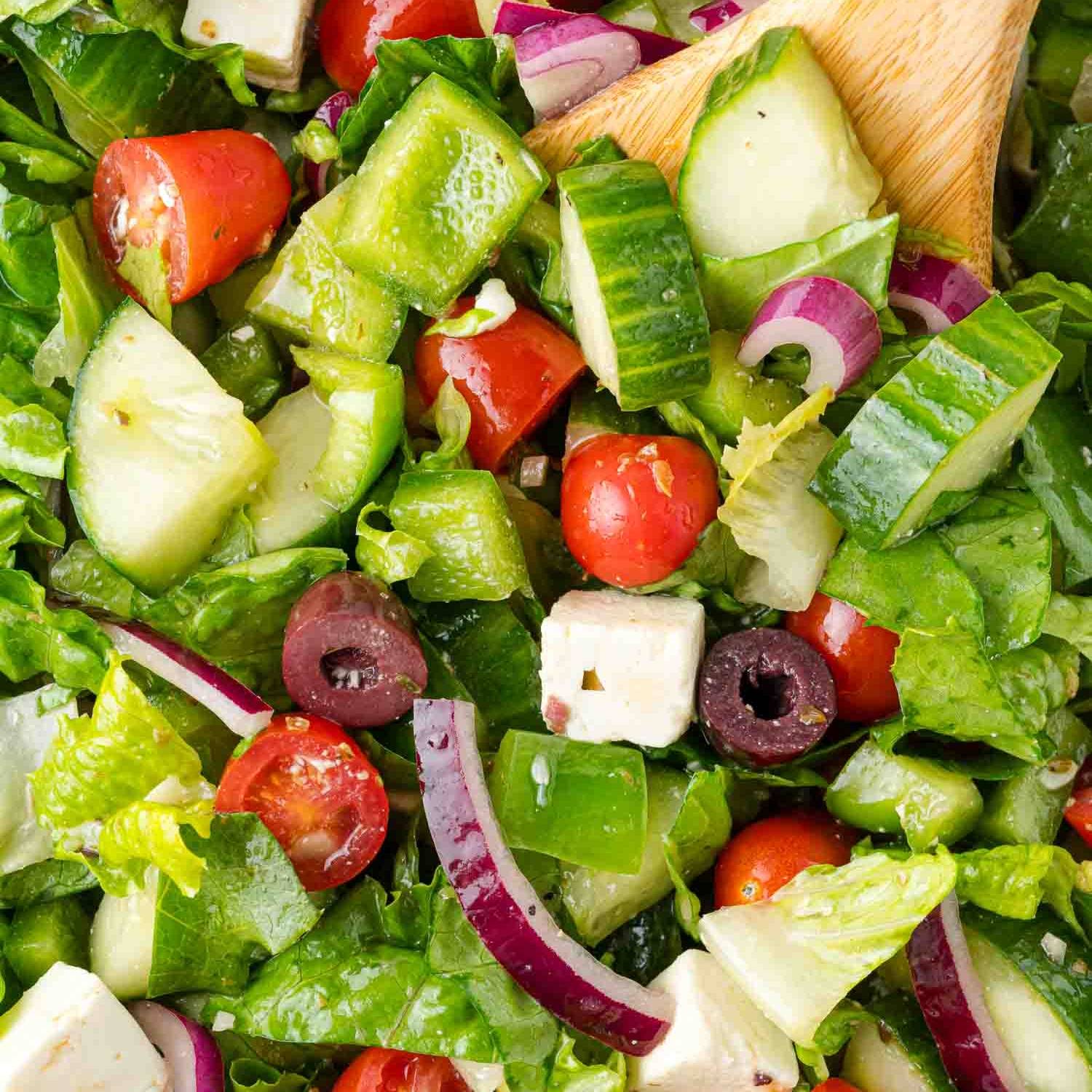 Close up of Greek salad, with a wooden spoon in it.