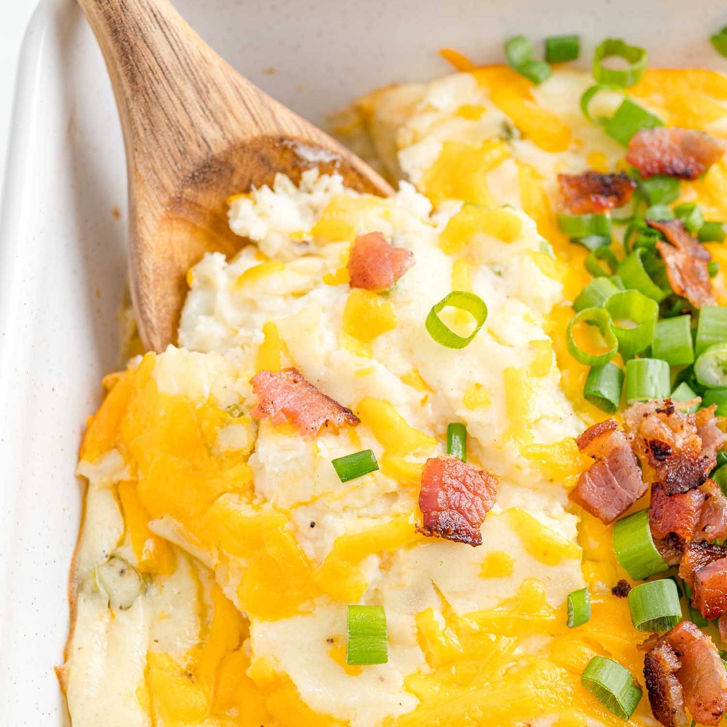 A mashed potato casserole topped with cheddar cheese, crisp bacon, and sliced green onions. 