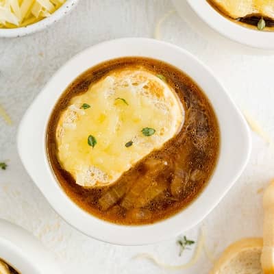 French onion soup in a bowl topped with cheesy bread piece.