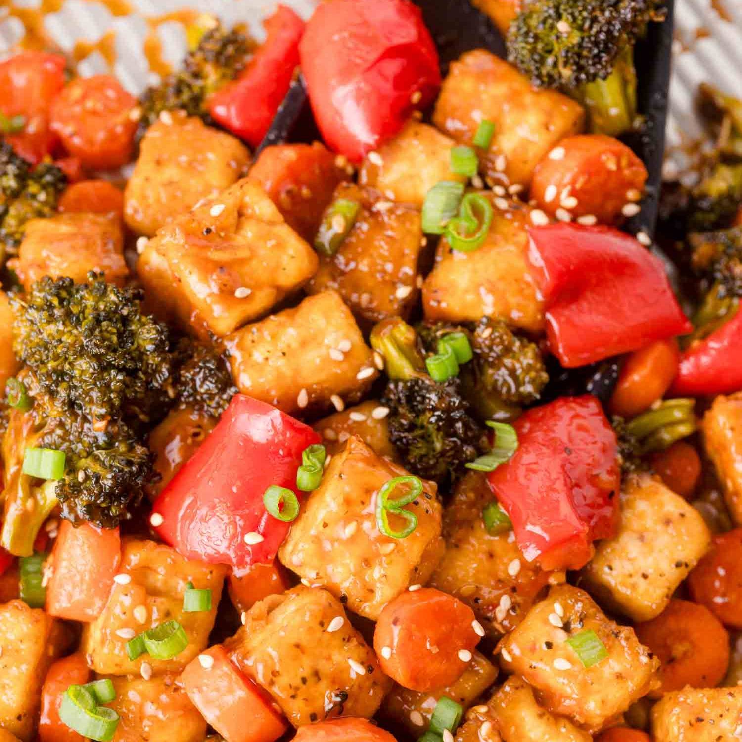 Tofu, broccoli, carrots, and red peppers in a brown sauce topped with green onions and sesame seeds.
