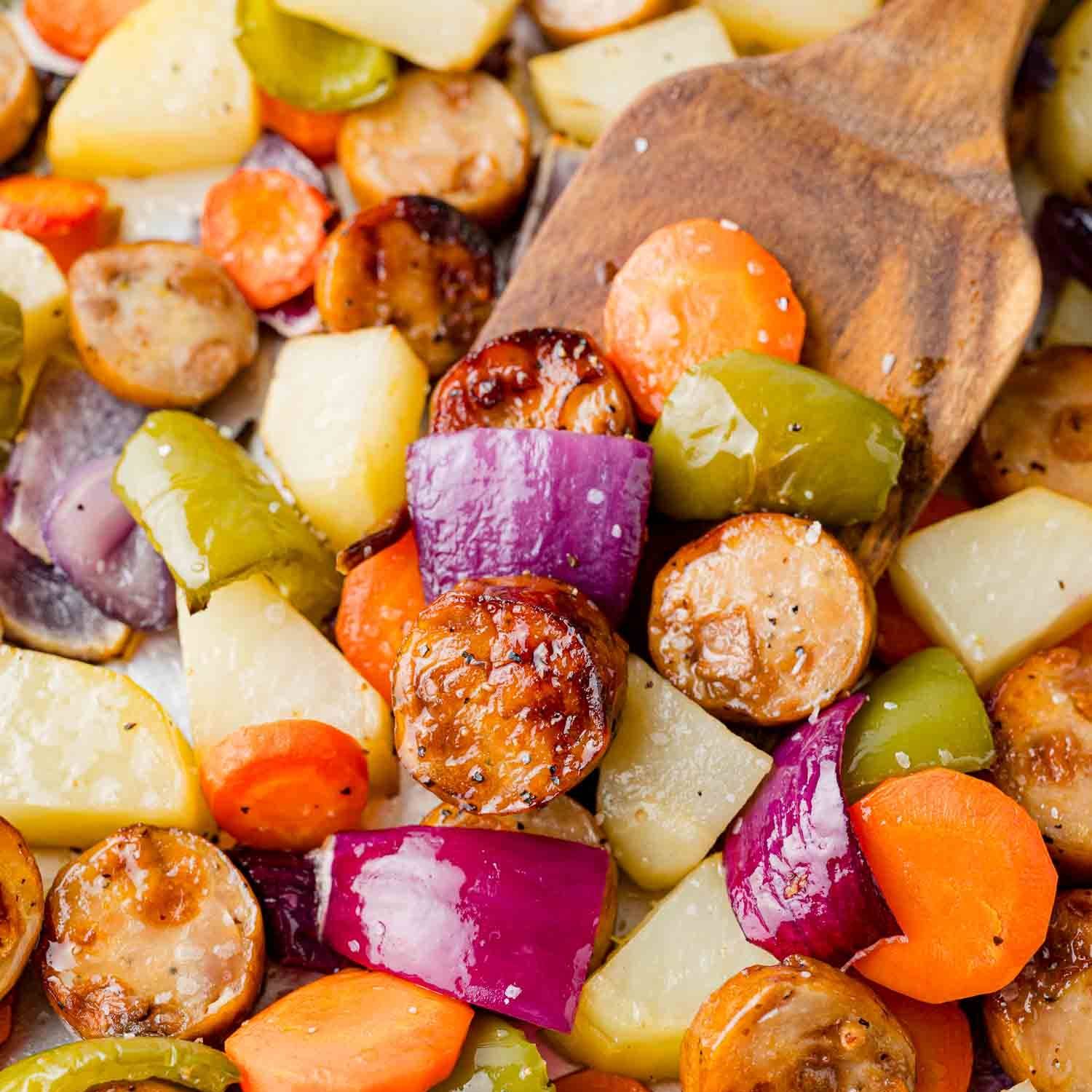 Sausage slices, pototatoes, and bell peppers, with a wooden server.