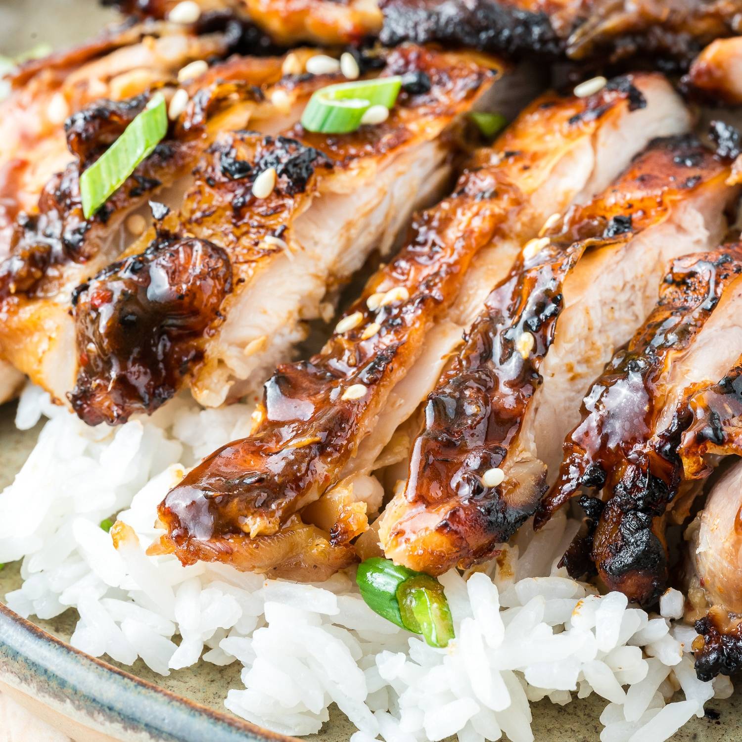 Ginger glazed chicken thigh sliced and served over rice, garnished with green onions.