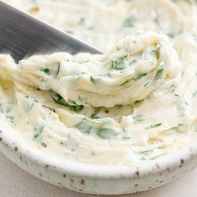 Garlic butter, with a knife scooping some out of a small dish.
