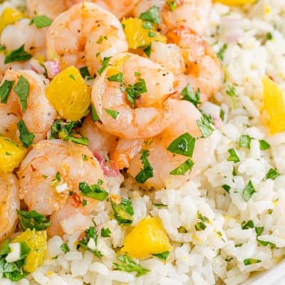 Shrimp with herbs and oranges on top of rice.