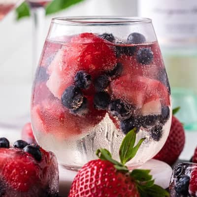 White wine spritzer in a stemless glass, with berry ice cubes.