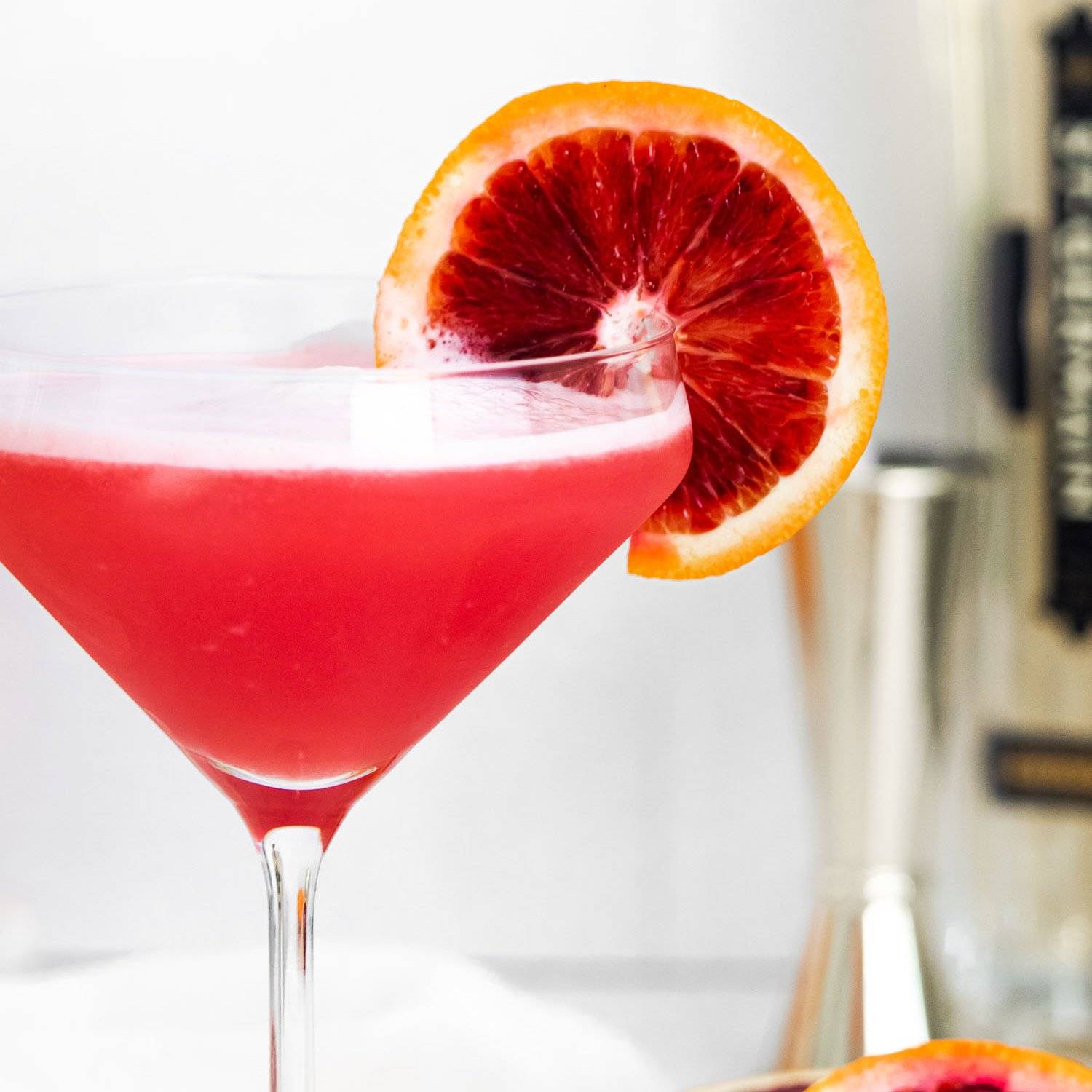 Reddish orange drink in a martini glass, garnished with a blood orange slice.
