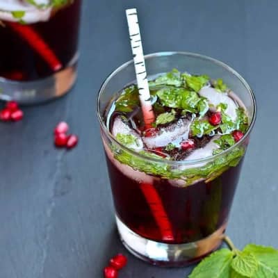 Dark red drink with ice, mint leaves, and pomegranate arils.