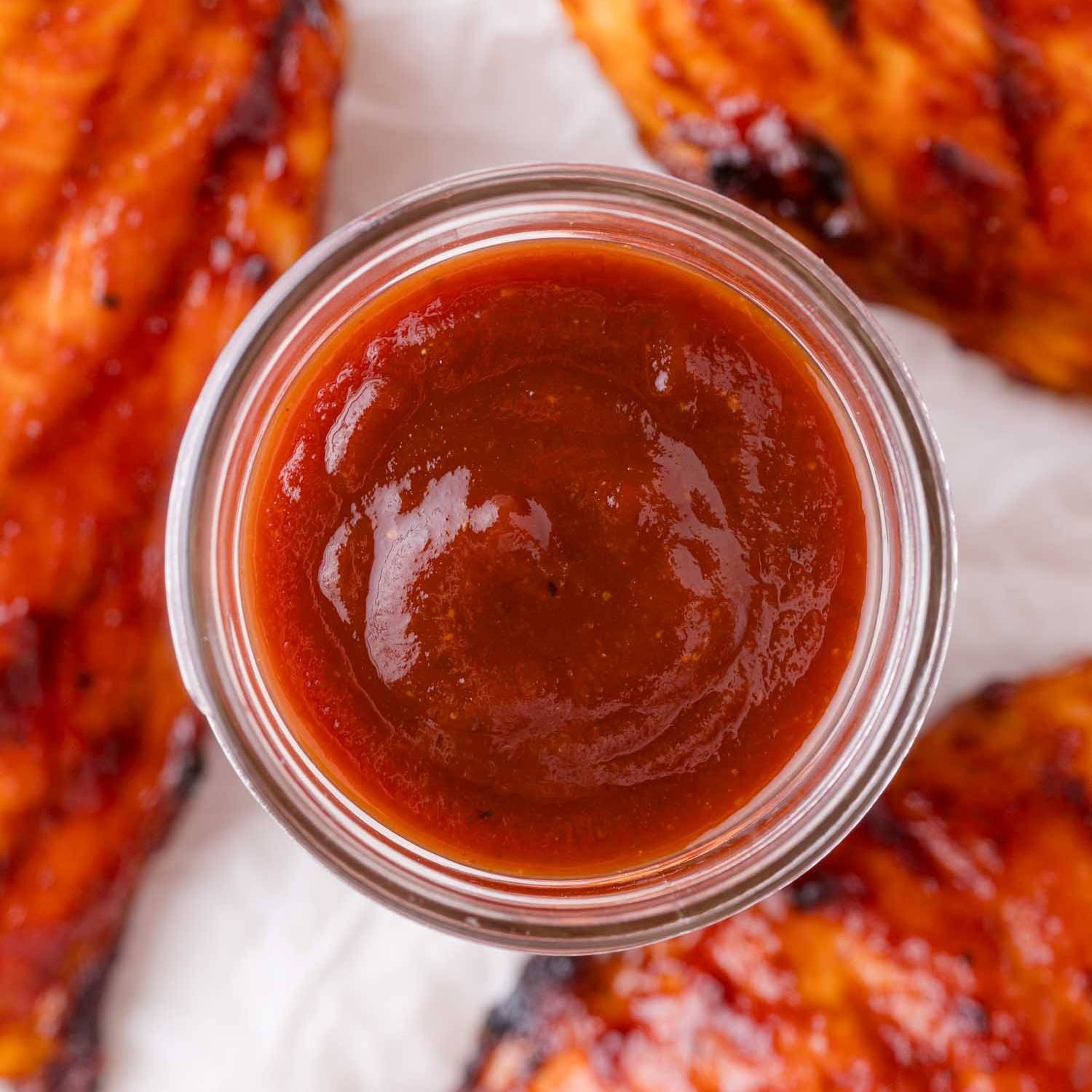BBQ Sauce in a small jar, surrounded by pieces of barbecued chicken.