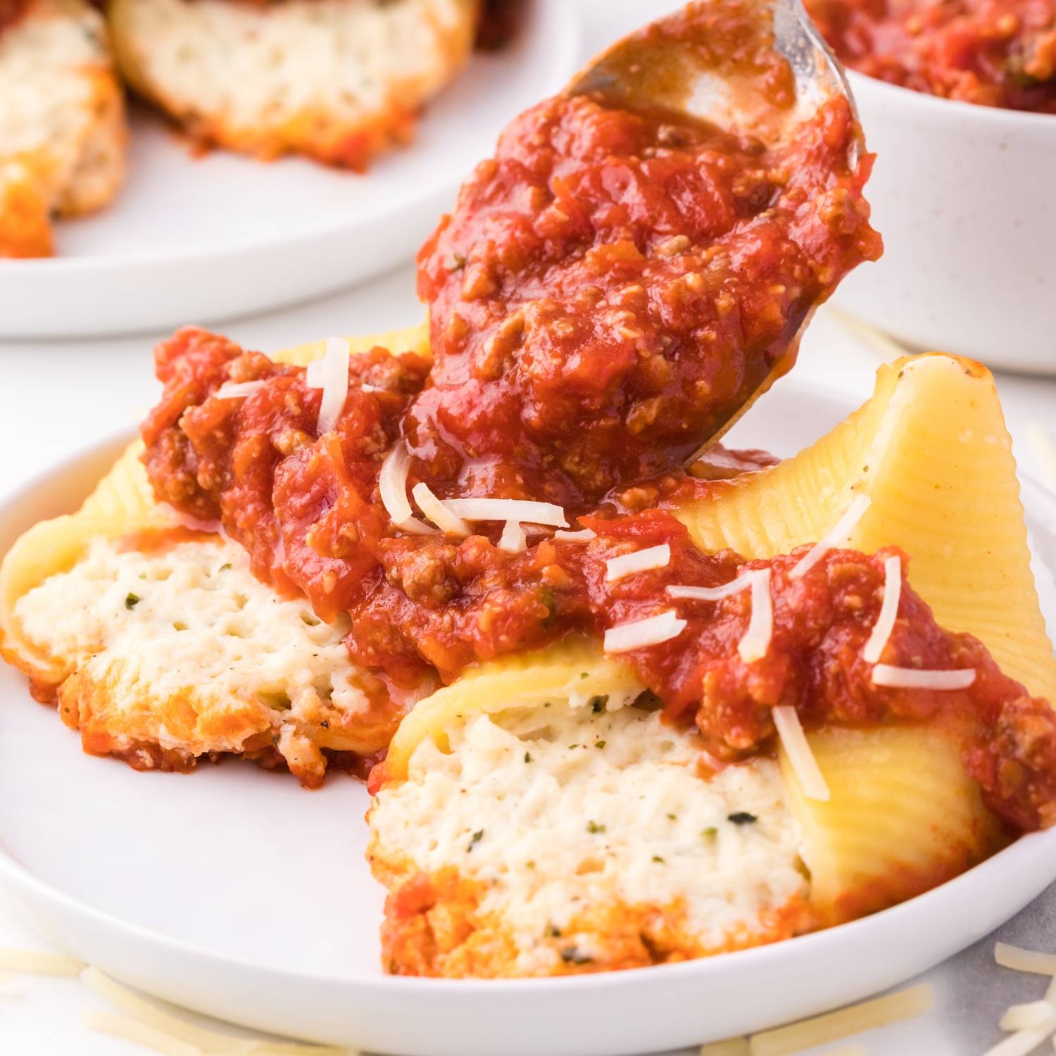 Two stuffed shells on a plate, being topped with meat sauce.
