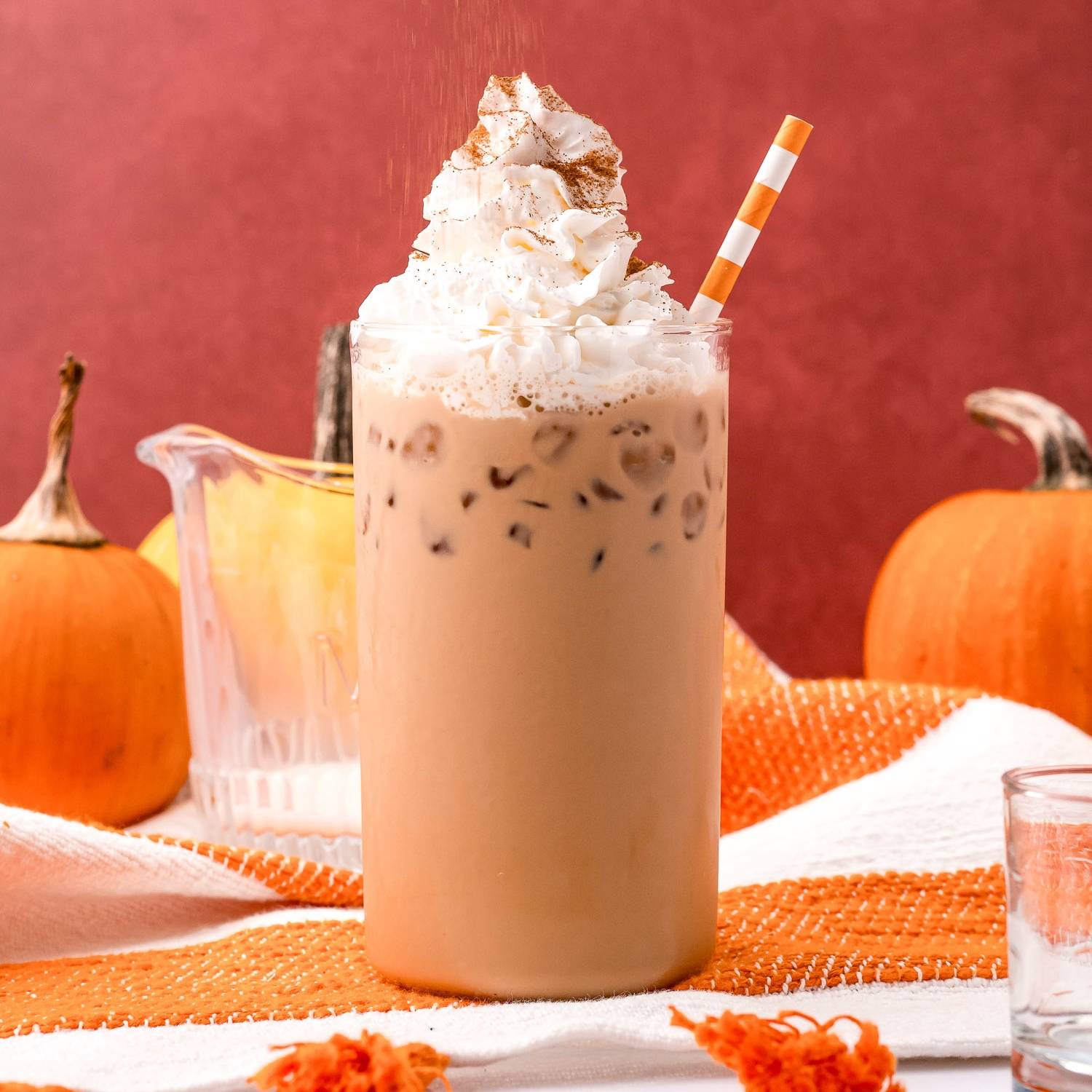 Pumpkin spice latte on ice in a tall glass with whipped cream on top.