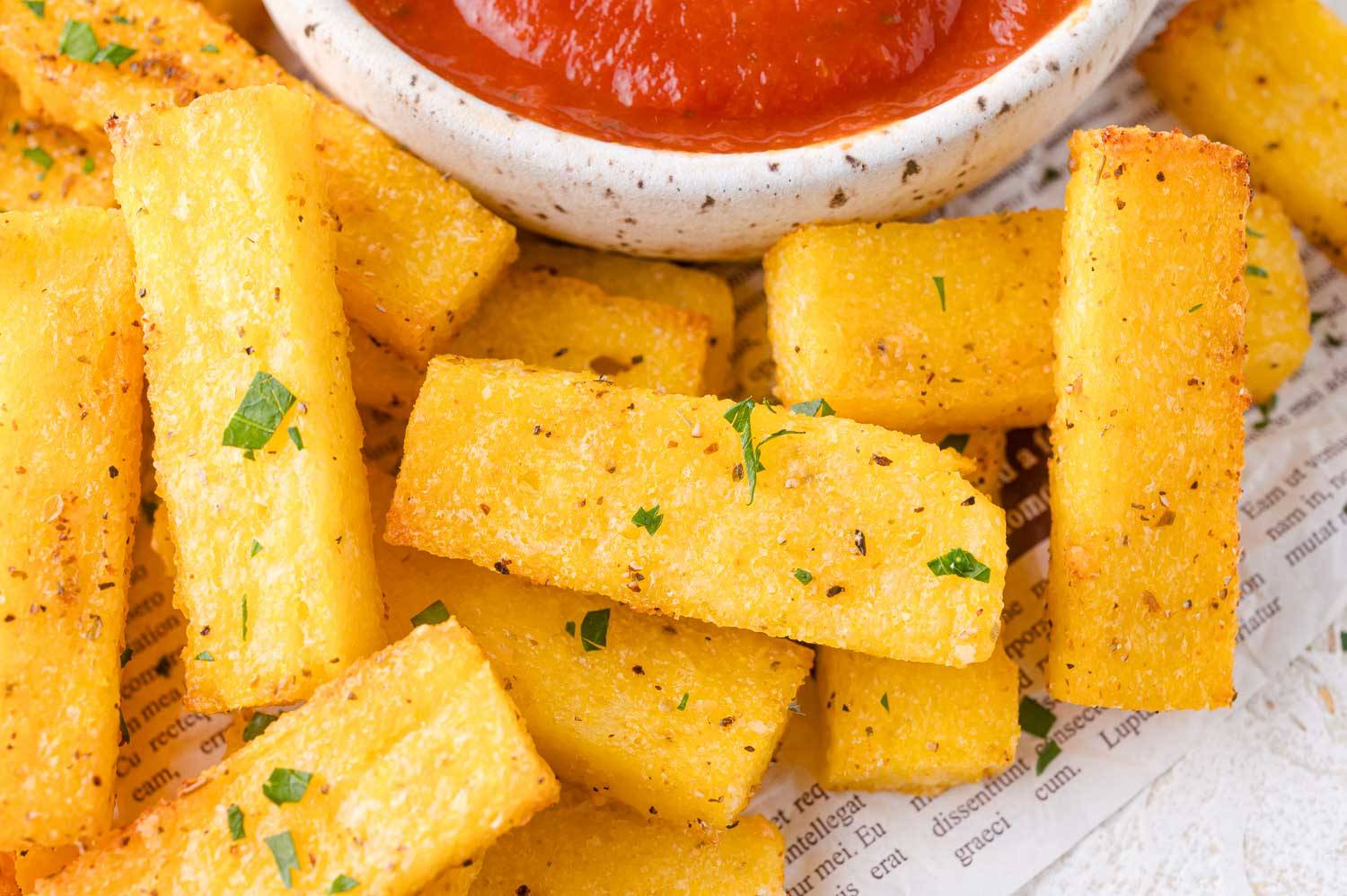 Polenta fries sprinkled with parsley, a small bowl of marinara partially visible.