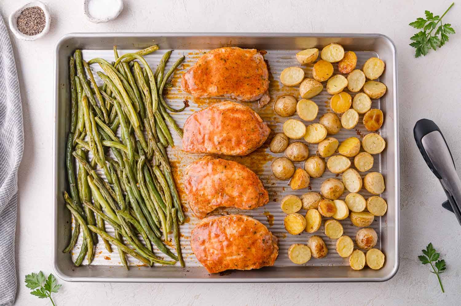 Pork chops, baby potatoes, and green beans on a sheet pan.