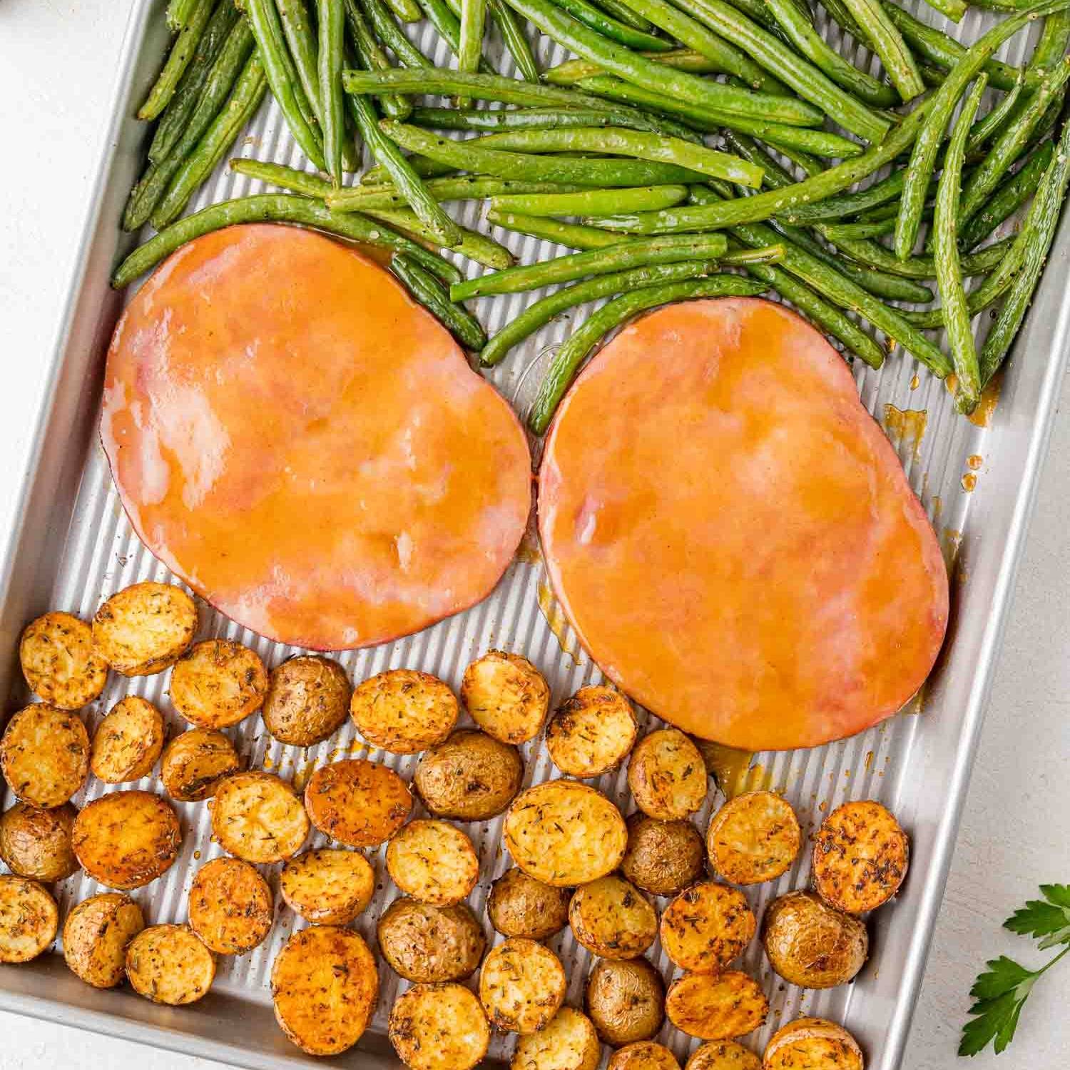 Ham steak, potatoes, and green beans on a sheet pan.