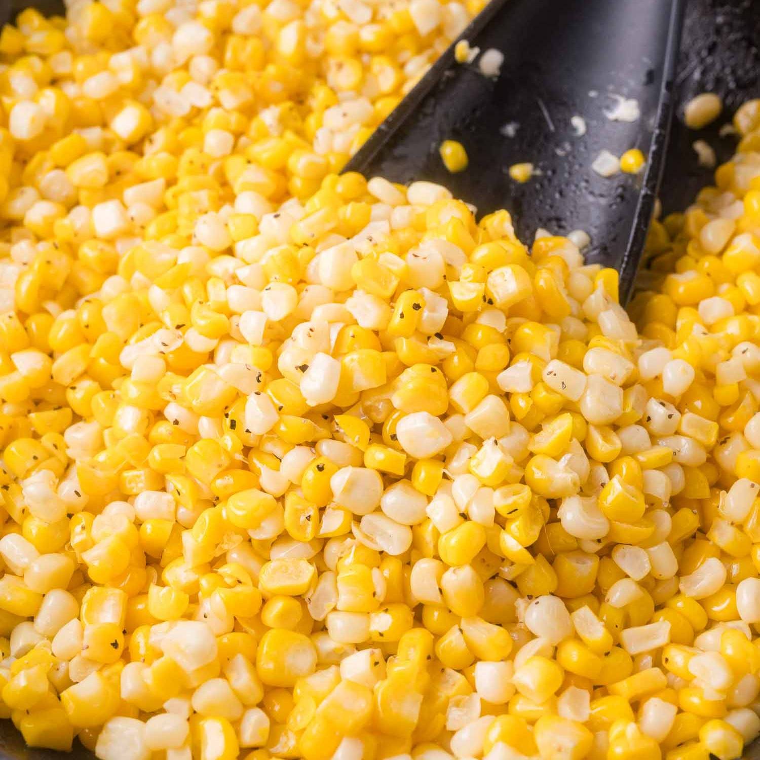 Fresh corn in a skillet with a black utensil stirring it.