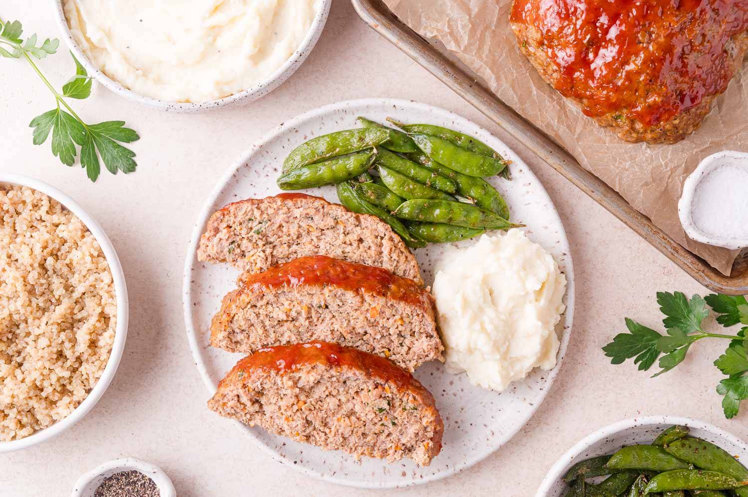 Three slices of meatloaf on a plate with sugar peas and mashed potatoes.