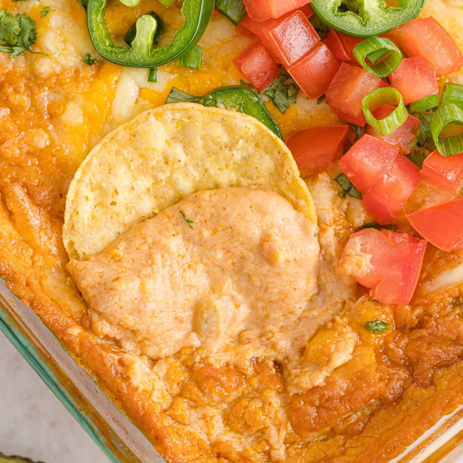 Refried bean dip, with a chip dipping into it to show creamy texture.