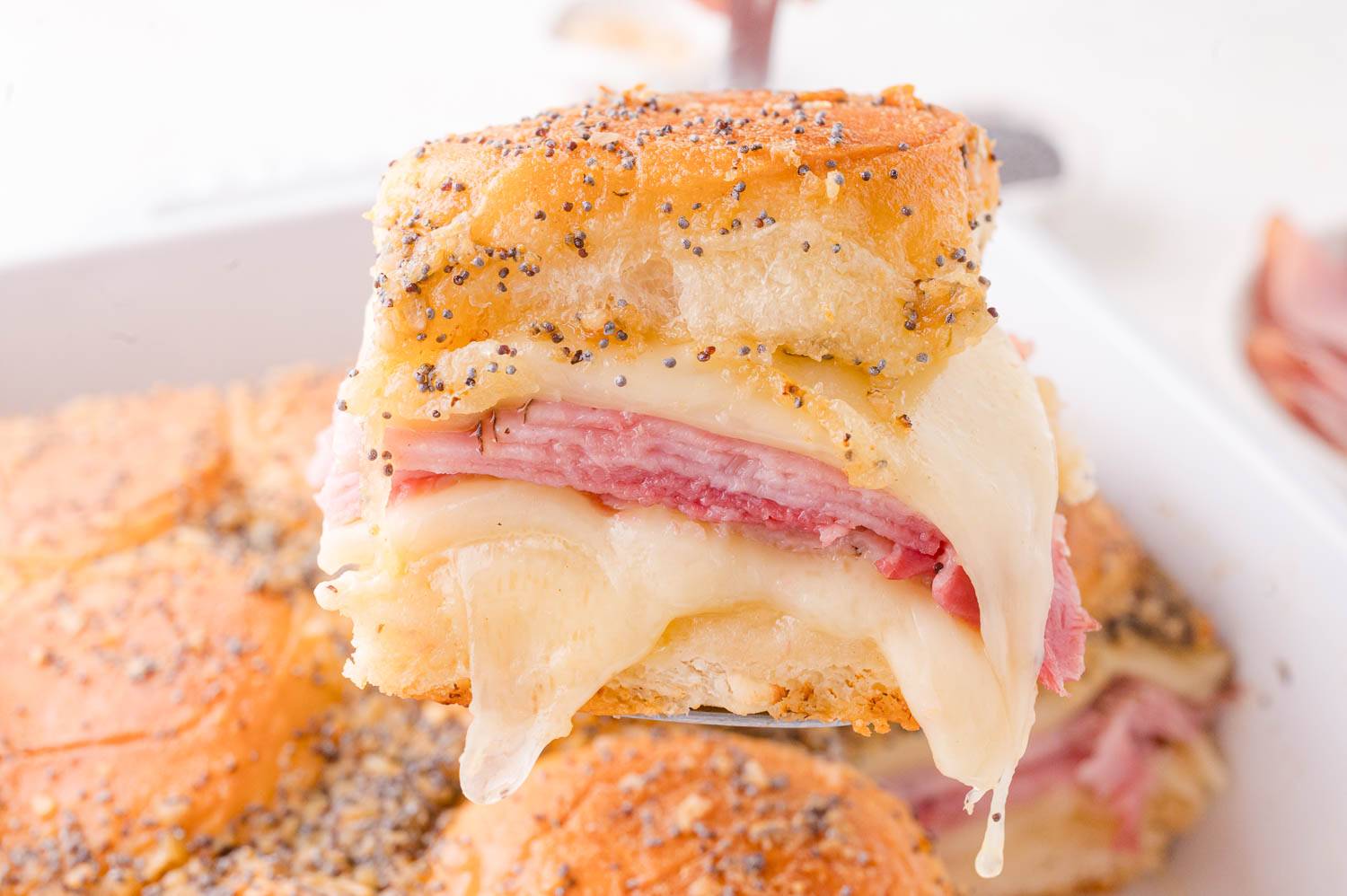 Ham and cheese slider being lifted from casserole dish.