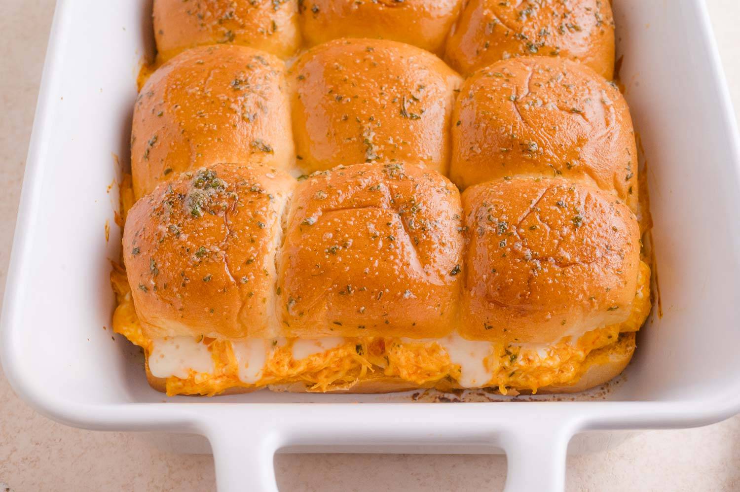 White pan filled with buffalo chicken sliders, topped with garlic butter.