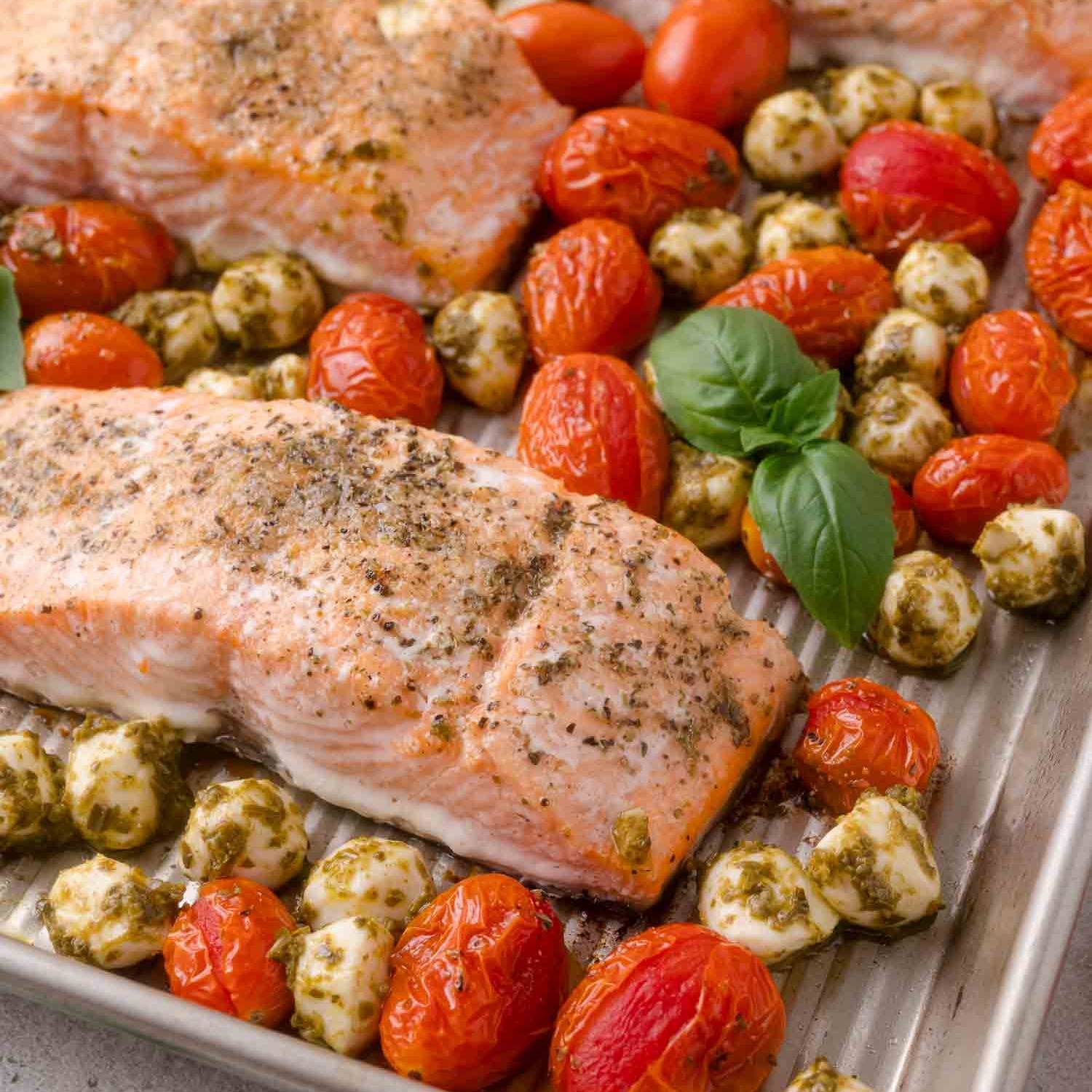 Salmon on a sheet pan with pesto coated mozzarella and roasted tomatoes.
