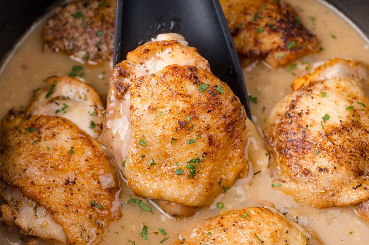 Braised chicken thighs in a pot, one being scooped out with a black spoon.